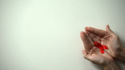 Red ribbon in female hands, world AIDS and HIV day, awareness campaign, closeup