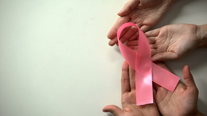People hands showing pink ribbon to camera, breast cancer prevention campaign