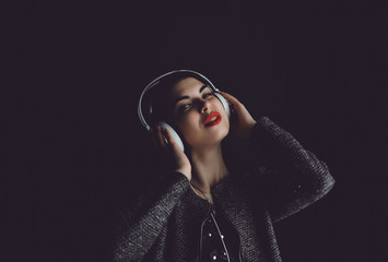 Beautiful young girl with brunette hair listening to music on headphones, street style, outdoor...