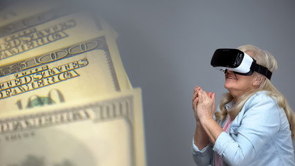 Elderly lady wearing VR headset happy with dollar banknotes, lottery concept