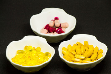 Capsules, tablets and gelatin-shaped medicines in oyster-shaped bowls on black background