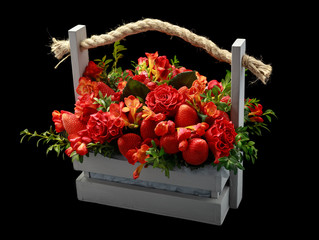 Unique handmade gift made up of ripe strawberries and red roses packed in a wooden box. Right view on black background.