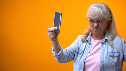 Happy old lady taking selfie on smartphone, showing grimace, modern technologies