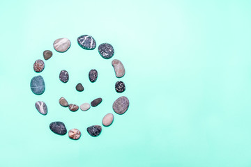 Beach pebbles made into a smiling face on a mint background. Concepts for health, happiness, healing, wellness. copy space. top view.