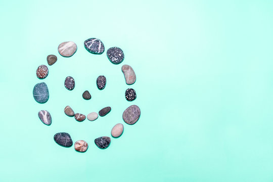 Beach pebbles made into a smiling face on a mint background. Concepts for health, happiness, healing, wellness. copy space. top view.