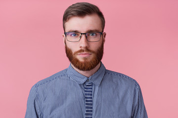 Close up of calm emotionless bearded young man in glasses, looking at the camera without emotion...