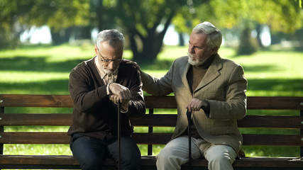 Old man supporting depressed friend, sitting in park near nursing home, lost