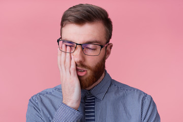 Portrait of young bearded man in glasses, tired of working and falling asleep, propping up his...