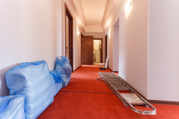 Bags with bed linen and ladder are on the floor of hallway in the hotel is under construction,...