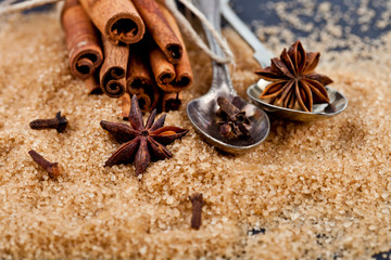 Brown cane sugar, cinnamon sticks and star anise closeup on black board background.
