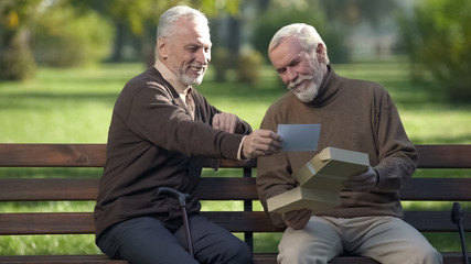Two male friends on park bench looking at photo and smiling, old time memory