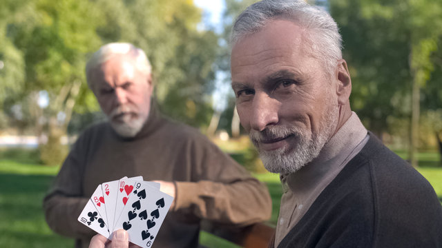 Two grandfathers playing cards on bench in park, weekend leisure, old age hobby