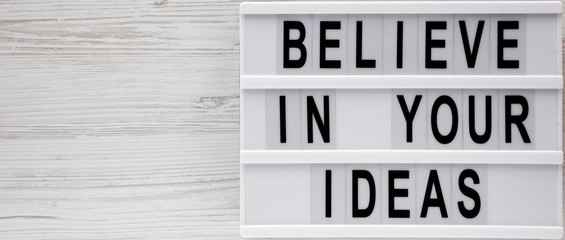'Believe in your ideas' words on modern board over white wooden background. Flat lay, from above, overhead. Copy space.