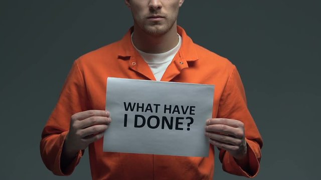What have I done question on cardboard in hands of Caucasian prisoner, sorrow