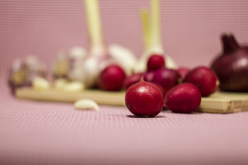 Healthy vegetables on a pink background. Fresh garlic (allium, Bulbus Allii Sativ) is a real storehouse of nutrients and trace elements. Red sweet onions (solaninum) - natural antioxidant. Red radish 