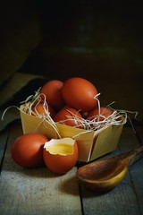 Many village eggs lie in a wicker basket in the chicken coop on the wooden floor.