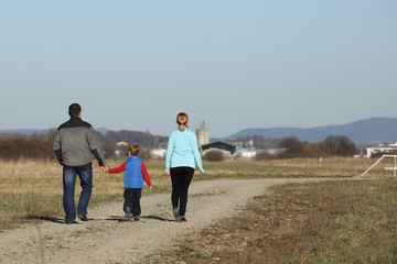 The family walks in nature on a dirt road stretching into the distance. Father mother and son spend free time together in the fall. Population activity in the fresh air in spring time. Parents
