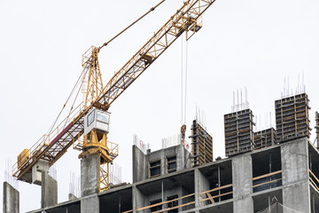 Fototapeta na wymiar High-rise building crane with a long arrow of yellow color against the sky above a concrete building under construction with brick walls
