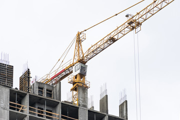 High-rise building crane with a long arrow of yellow color against the sky above a concrete building under construction with brick walls