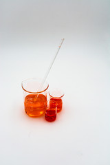 Vertical image with three science beakers filled with orange and red fluid with a stirring rod on a white background with natural shadows