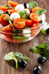Fresh tomato, cheese and spinach salad on wooden background. Healthy diet.