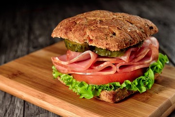 resh sandwich with ham, cheese, bacon, tomatoes, salad, cucumbers and onions on a wooden cutting Board