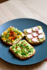 Three slices of toast with mashed avocado and various vegetable and herb toppings. Selective focus.