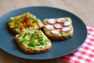 Three slices of toast with mashed avocado and various vegetable and herb toppings. Selective focus.