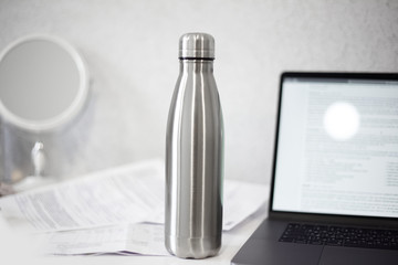 Steel thermo bottle for water on office table near laptop and documents.