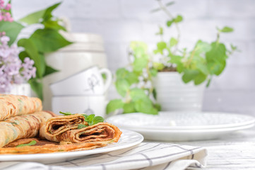 Pancakes with dill and white sauce on a light background. Spring flowers and tableware for breakfast.