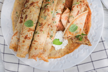 Pancakes with dill and white sauce on a light background. top view.