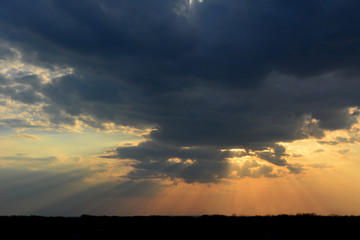 Beautiful sunset sky with dramatic light. Sun rays through dark clouds.