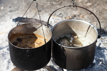 Cooking in two sooty old cauldrons on campfire