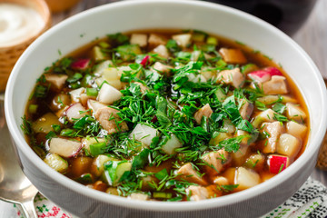 Traditional Russian summer cold soup okroshka with kvass in bowl on wooden background. Selective focus.