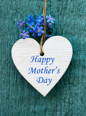 Happy Mother's Day greeting card with decorative white heart and forget-me-not flowers on old blue wooden background.Spring holidays concept.