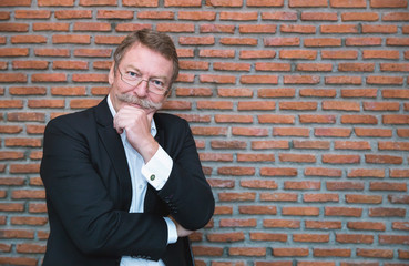 Portrait of confident success senior businessman standing on orange old brick wall. Elderly entrepreneur rich man gesture like a big boss. Business management successful owner concept