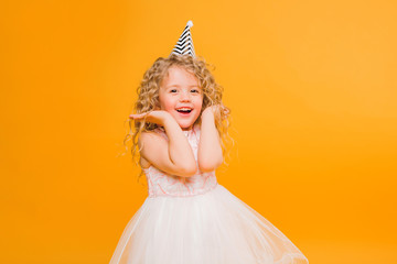 Young blond girl in birthday party princess hat hands spread up screaming isolated on a yellow background,Young beautiful girl wearing birthday cap over isolated background smiling with happy face © Tina kids photo