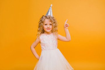 Young blond girl in birthday party princess hat hands spread up screaming isolated on a yellow background,Young beautiful girl wearing birthday cap over isolated background smiling with happy face