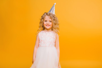 Young blond girl in birthday party princess hat hands spread up screaming isolated on a yellow background,Young beautiful girl wearing birthday cap over isolated background smiling with happy face