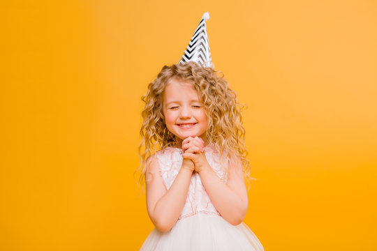 Young blond girl in birthday party princess hat hands spread up screaming isolated on a yellow background,Young beautiful girl wearing birthday cap over isolated background smiling with happy face