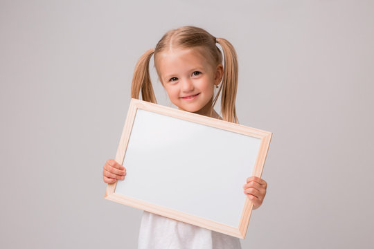 girl holding a white Board .Cute little girl with a white sheet of paper.white background.copy spase.Little girl holding an empty white sheet,place for text