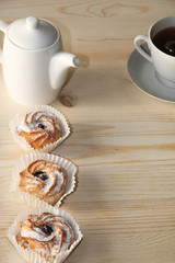 Chocolate muffins and a cup of coffee on a wooden background, close-up. Selective focus. Delicious muffins sprinkled with powdered sugar in paper cups