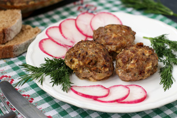 Meat patties and radish on a white plate against a dark background