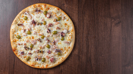 Pizza with seafood on a wooden table top view next to the copy space.