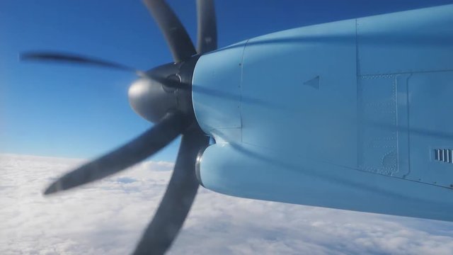 Detail of spinning propeller on plane wing, flying over white fluffy sky on blue serene sky