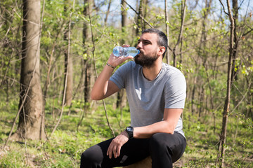 Naklejka na ściany i meble Portrait of handsome young man athlete drinking water in forest