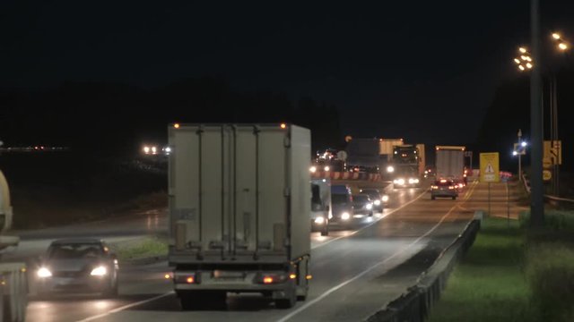 Cars and trucks on the highway. Suburban car traffic on the road at night. Dark forest in the background. Night lighting. Lanterns at night along the road. Dark background. Blue sky.