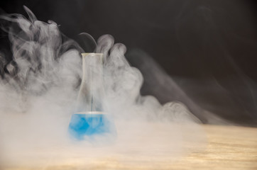 flask with blue liquid in smoke over black background. chemical analysis