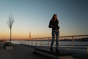 Fototapeta premium Young woman feeling confident during a lifestyle walk along the River Daugava at a sunset
