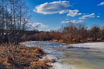 Early Spring landscape melts ice on a small river at the edge of the village.